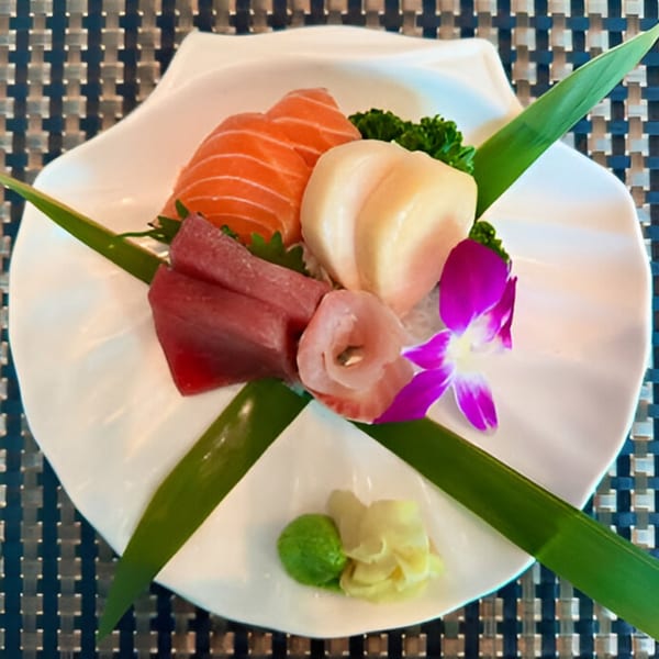Assorted sashimi, including salmon, tuna, and white fish, garnished with an orchid and bamboo leaves.