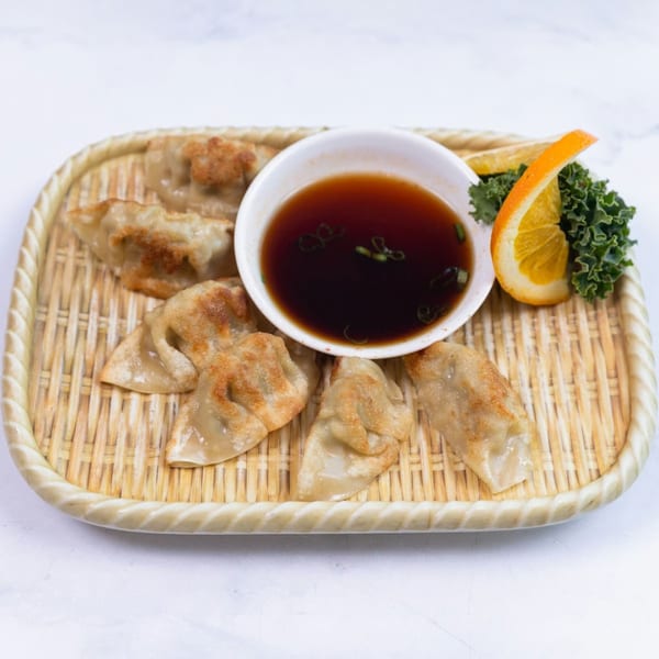 Pan-fried gyoza dumplings with a side of soy dipping sauce, garnished with orange and greens.