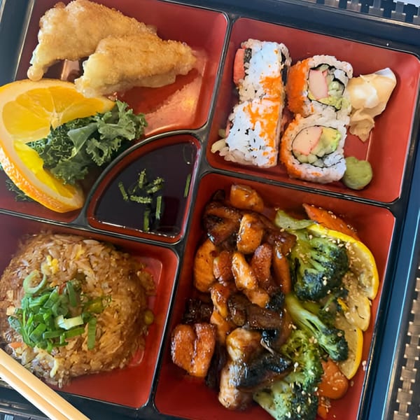 A Tsukino Sushi Bar bento box with sushi, fried shrimp, teriyaki chicken, fried rice, and vegetables.