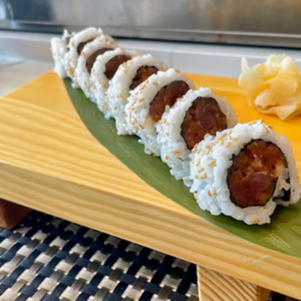 A row of Tsukino Sushi Bar's tuna sushi rolls with sesame seeds and pickled ginger on a wooden board.