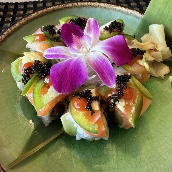 Tsukino Sushi Bar's sushi rolls with salmon, avocado, caviar, and a purple orchid on a green plate.