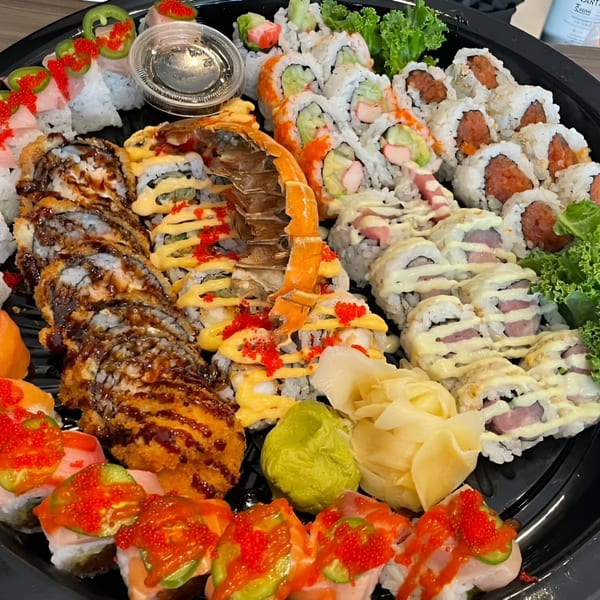 A large platter of assorted sushi rolls, including deep-fried, spicy, and lobster tail options, with ginger and wasabi.