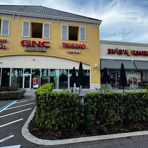Exterior view of Tsukino Sushi Bar, a yellow building with outdoor seating under black umbrellas.