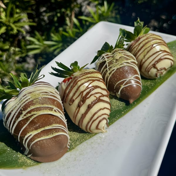 Four chocolate-dipped strawberries, two dark and two white, drizzled with contrasting chocolate and matcha powder.