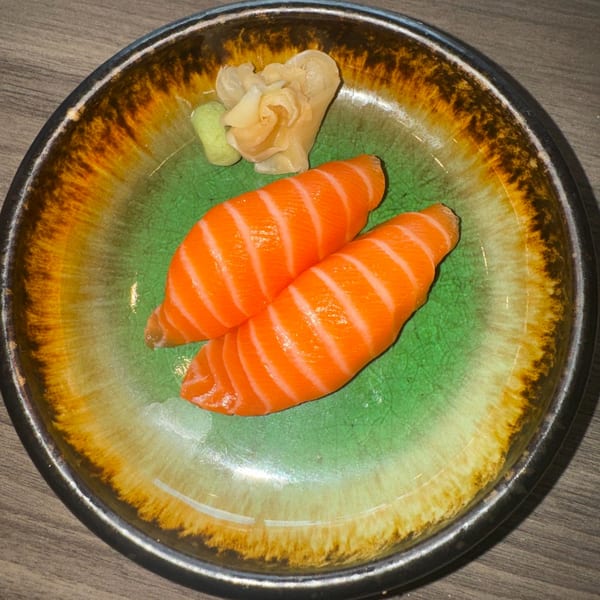 Two pieces of salmon nigiri sushi with ginger and wasabi on a green and brown plate.